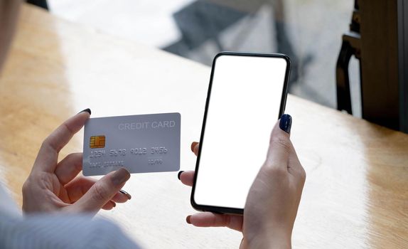 Online payment. woman holding smartphone with blank screen and credit card, making financial transaction.