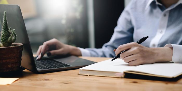 Hands of financial manager taking notes when working on report.