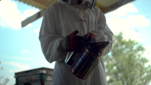 A beekeeper with a bee smoker to neutralize bees in his hands. A man in a special protective suit in the apiary. 4k