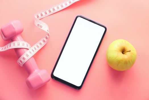 healthy diet concept with smart phone, apple and dumbbell on pink background .