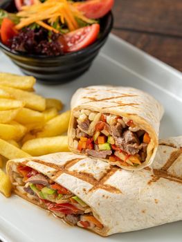 Meat wrap cut in half with french fries on dark stone table