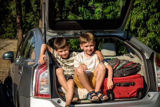 Two cute boys sitting in a car trunk before going on vacations with their parents. Two kids looking forward for a road trip or travel. Summer break at school. Family travel by car.