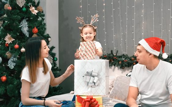 Cozy family christmas, father mother and child girl daughter play and have fun with gifts in bedroom, happy cheerful xmas holiday together, authentic festive lifestyle, gray interior