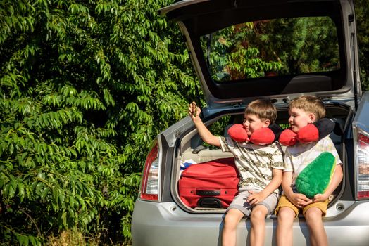 Two adorable little kids boy sitting in car trunk just before leaving for summer vacation. Sibling brothers making selfie on smartphone. Happy family going on long journey.