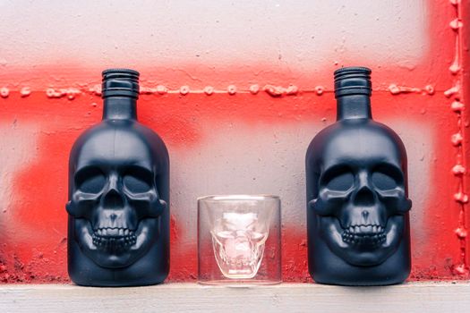 glass gin bottles in the shape of a human skull and a glass stack in the shape of a skull. Drink for a night party on a gray metal background