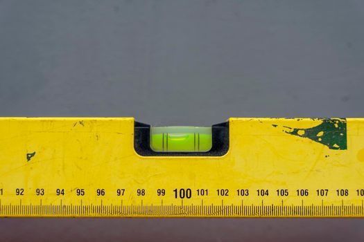 an iron yellow bubble construction level with a length marking on a gray background in a horizontal position. Close-up. Space for copying. Leader. Construction and engineering equipment. Measure