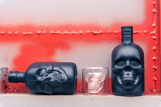 glass gin bottles in the shape of a human skull and a glass stack in the shape of a skull. Drink for a night party on a gray metal background