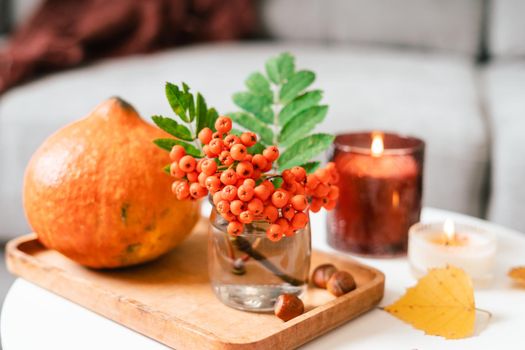 Still life book, candle, rowan berry, pumpkin and a cup of tea or coffee in the living room on a table, home decor in a cozy house. Autumn weekend concept, plaid. Fallen leaves and home decoration