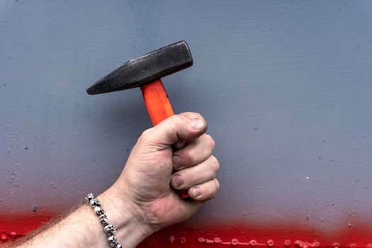 male hand holding a hammer with a short plastic handle on gray background