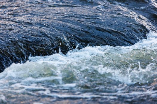 flowing water of a summer river with a small rapid waterfall at evening light, short or fast shutter speed