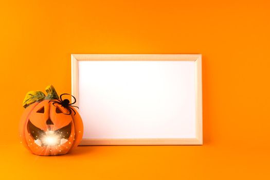 Halloween holiday concept. Jack o lantern with light bokeh, handmade paper decorations, spider and blank frame on orange background. Halloween festival party, greeting card with mockup copy space.