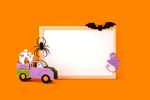 Halloween holiday concept. Halloween handmade paper decorations, spider, ghosts in car, bat and blank frame on orange background. Halloween festival party, greeting card with mockup copy space.