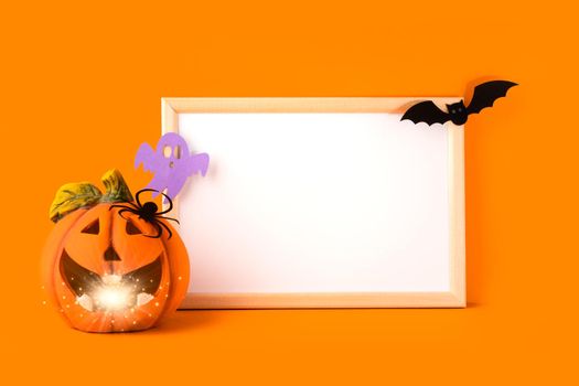 Halloween holiday concept. Jack o lantern, light, handmade paper decorations, spider, ghost, bat and blank frame on orange background. Halloween festival party, greeting card with mockup copy space.