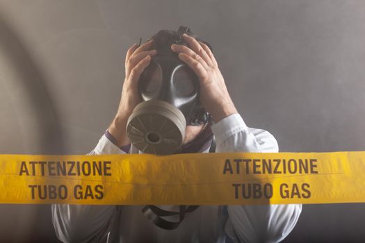 A medical engineer wearing antigas mask experienced in the gas leaks crisis directing the emergency during the chaos. On the yellow tape the written notice "attention gas tube"