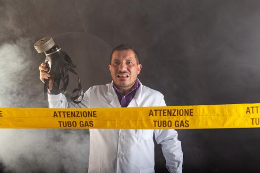 A medical engineer with an antigas mask on his hand directs the emergency in the chaos during the gas leaks. On the yellow tape the written notice "attention gas tube"