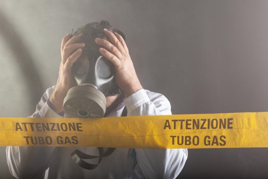 A medical engineer wearing antigas mask experienced in the gas leaks crisis directing the emergency during the chaos. On the yellow tape the written notice "attention gas tube"