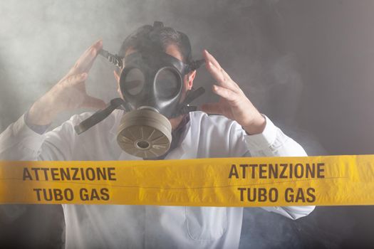 A medical engineer wearing an antigas mask during the gas leaks crisis and the emergency during the chaos. On the yellow tape the written notice "attention gas tube"