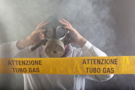 A medical engineer wearing antigas mask experienced in the gas leaks crisis directing the emergency during the chaos. On the yellow tape the written notice "attention gas tube"