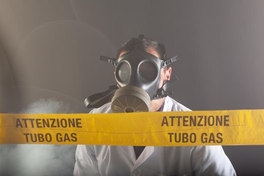 A medical engineer wearing antigas mask experienced in the gas leaks crisis directing the emergency during the chaos. On the yellow tape the written notice "attention gas tube"