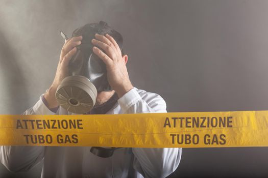 A medical engineer wearing an antigas mask during the gas leaks crisis and the emergency during the chaos. On the yellow tape the written notice "attention gas tube"