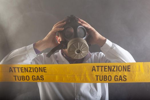 A medical engineer wearing antigas mask experienced in the gas leaks crisis directing the emergency during the chaos. On the yellow tape the written notice "attention gas tube"