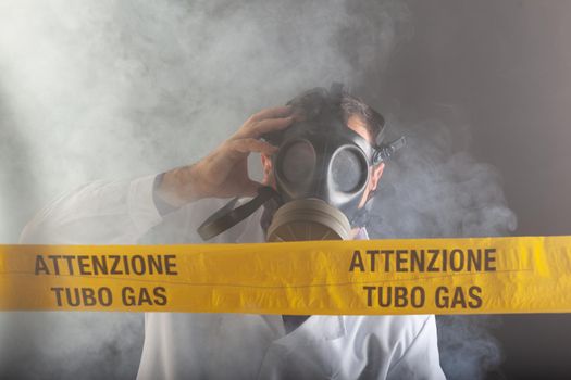 A medical engineer wearing antigas mask experienced in the gas leaks crisis directing the emergency during the chaos. On the yellow tape the written notice "attention gas tube"