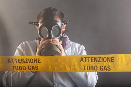 A medical engineer wearing antigas mask experienced in the gas leaks crisis directing the emergency during the chaos. On the yellow tape the written notice "attention gas tube"