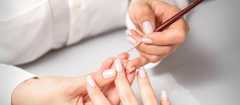 French manicure. Manicure master drawing white varnish on the nail tip with a thin brush, close up