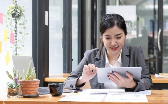 Beautiful smiling Asian businesswoman wearing glasses hand holding pen working using tablet at office