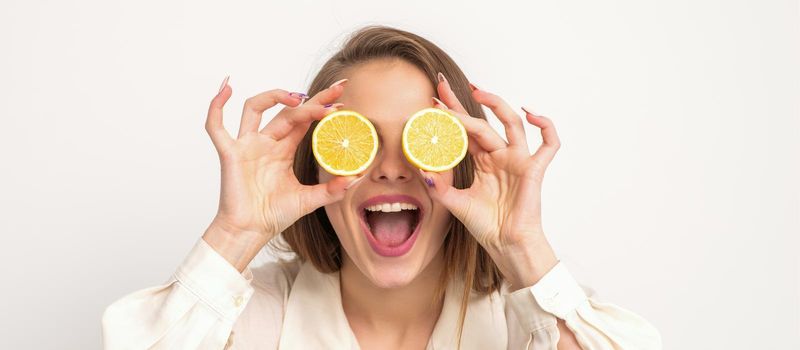 Portrait of a beautiful young woman with an open mouth holding two slices of orange at her eyes against a white background