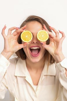 Portrait of a beautiful young woman with an open mouth holding two slices of orange at her eyes against a white background