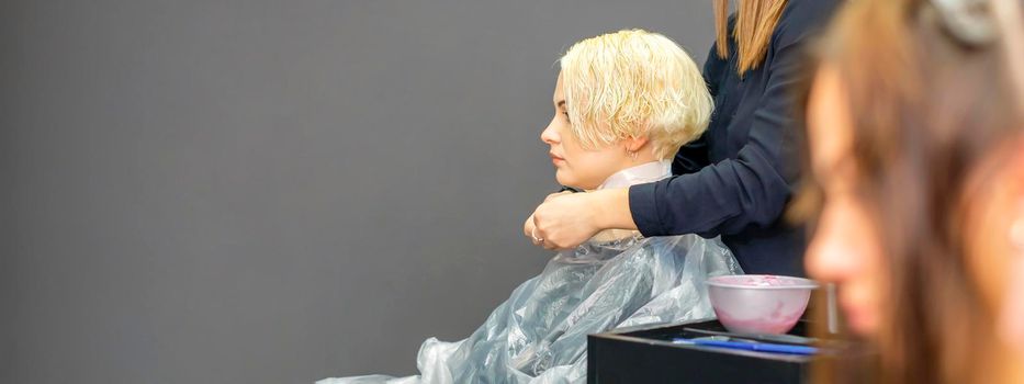 The female hairdresser puts on a transparent cellophane cape to the female client in a beauty hair salon