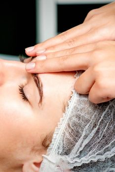 Side view fingers of female therapist making anti-age massage of forehead wrinkles to young caucasian woman in spa beauty salon