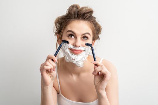 Beautiful young caucasian smiling woman shaving her face with razor looking up on white background