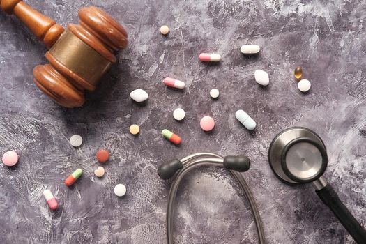 Top view of gavel, stethoscope and pills on black background.