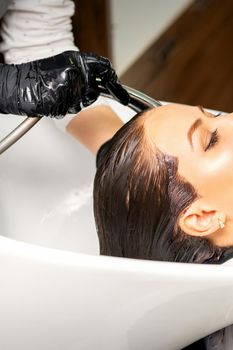 Male hairdresser washing hair in the sink to the female client before making hairstyling in a beauty salon