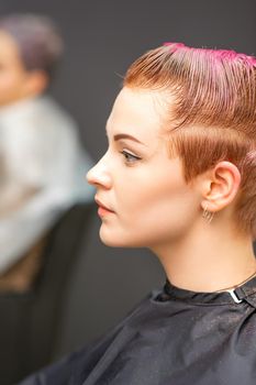 Side view portrait of a beautiful young caucasian woman with a short pink haircut waiting for a hairdresser in a beauty salon