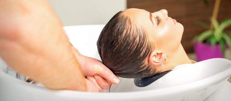 Male hairdresser washing hair in the sink to the female client before making hairstyling in a beauty salon