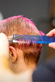 Young caucasian woman with pink hair getting a short haircut by a male hairdresser's hands in a hairdressing salon