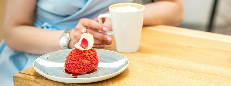 Young female drinking coffee with a piece of cake sitting at the table in a cafe outdoors