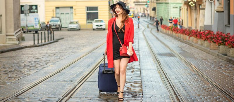 Beautiful young caucasian woman walks with a suitcase on a wet tram track in the European city