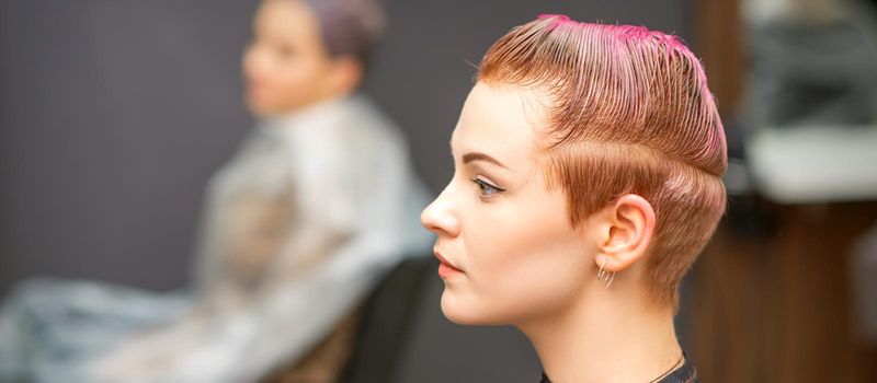 Side view portrait of a beautiful young caucasian woman with a short pink haircut waiting for a hairdresser in a beauty salon