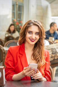 Beautiful young travel woman with smartphone sitting at the table looking at camera in cafe outdoors