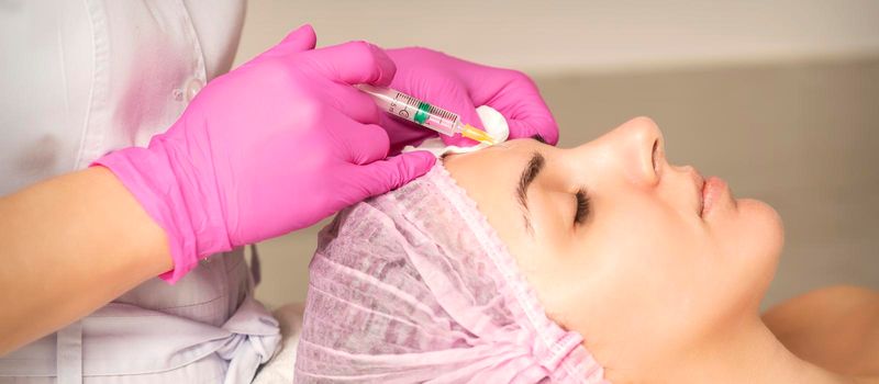 Young woman receiving an injection of anti-aging botox filler to the forehead from a cosmetologist in a beauty salon. Facial treatment injection