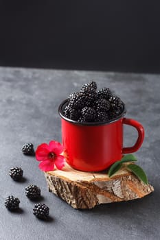 Fresh blackberry in a mug on a wooden stand on a black background with a flower. The concept of natural food. copy space