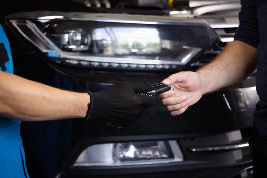 Close up shot of hands of mechanic giving car key to male client after servicing in auto repair shop. Car repair. Vehicle breaks down.