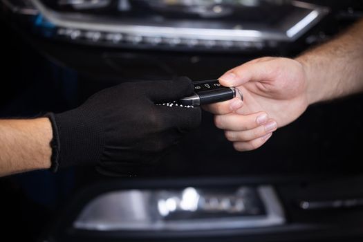 Car repair. Man owner of the auto gives the keys to the car repairman. Vehicle breaks down. Close up shot of hands of male client giving car key to mechanic in auto repair shop