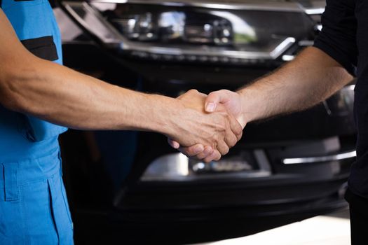 Automotive mechanic repairman handshake with client in garage. Vehicle service manager working in mechanics workshop. Success after check and maintenance car engine for customer. Car repair.