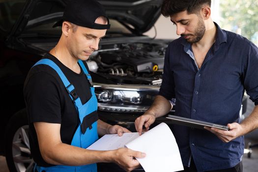 Car Service Employees Inspect the Bottom and Skid Plates of the Car. Manager Checks Data on a Tablet Computer and Explains the Breakdown to Mechanic. Specialist is Showing Info on Tablet