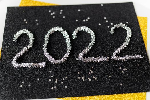 The year 2022 is written in New Year's silver tinsel on a black background along with silver stars. Greeting card
